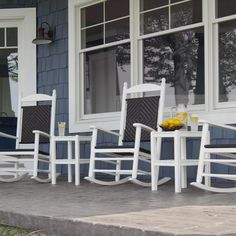 four white rocking chairs sitting on a porch next to a building with windows and doors