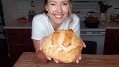 a woman is holding a large loaf of bread in front of her face and smiling at the camera