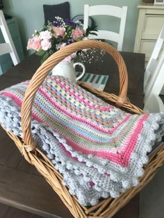 a basket with a blanket on top of it sitting on a table next to a vase