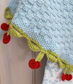 a blue and green knitted blanket with red pom - poms hanging from it