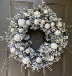 a wreath with silver and white ornaments hanging from it's side on a door