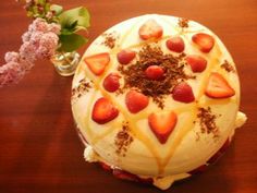 a cake with strawberries on top sitting on a table next to a vase filled with flowers