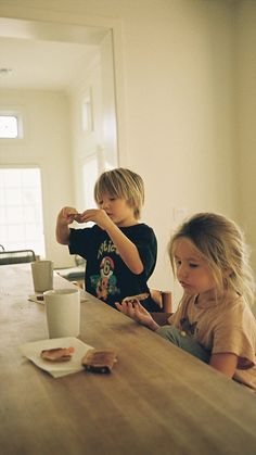 two young children sitting at a table with donuts and coffee in front of them