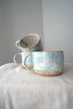 two blue cups sitting on top of a white tablecloth covered bed next to each other