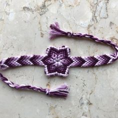 a purple and white bracelet with tassels sitting on top of a marble surface