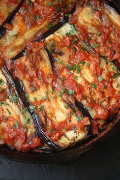 an eggplant dish with tomato sauce in a skillet on a black surface