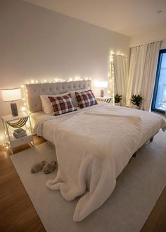 a white bed sitting in a bedroom next to a window with christmas lights on it