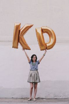 a woman holding up two gold balloons in the shape of letters k and person's initials