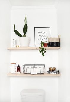 two shelves with plants and other items on them in a white bathroom, along with a toilet