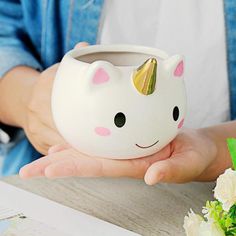 a person holding a white ceramic cup with a gold horn on it's face