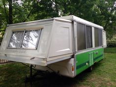 an old camper trailer is parked in the grass near some trees and fenced in area