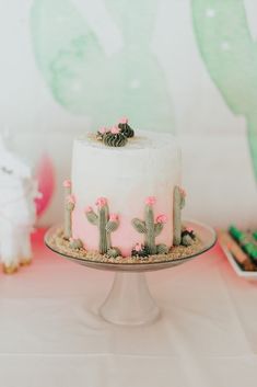 a white cake with pink frosting and cactus decorations on top is sitting on a table