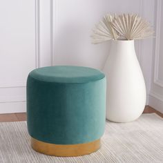 a white vase sitting next to a teal colored stool on top of a rug