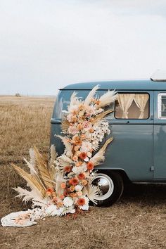 an old vw bus with flowers and feathers on the front parked in a field