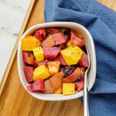 a white bowl filled with fruit on top of a wooden cutting board next to a blue towel