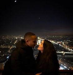 a man and woman standing next to each other in front of a city at night