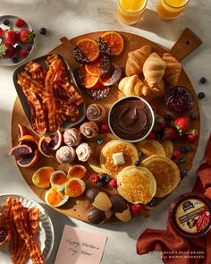 an assortment of breakfast foods are arranged on a wooden platter, along with orange juice and bacon