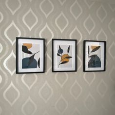 three framed pictures hang on the wall in front of a patterned wallpapered wall