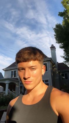 a young man standing in front of a house wearing a tank top and looking at the camera