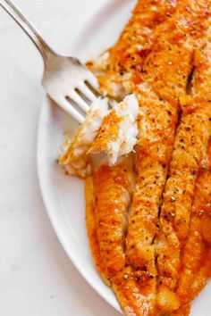 a white plate topped with fish covered in sauce and mashed potatoes next to a fork