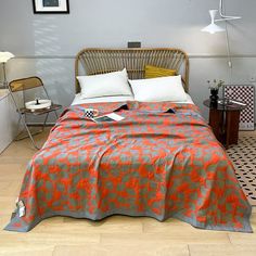 a bed with an orange and grey bedspread on it in a bedroom next to a chair