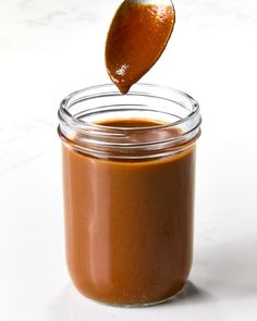 a spoon full of peanut butter on top of a jar filled with caramel sauce