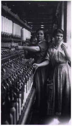 two women standing next to each other in front of an assembly line with rows of machines