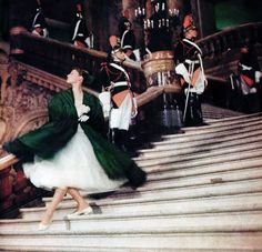 a woman in a green dress is walking down the stairs with other people behind her