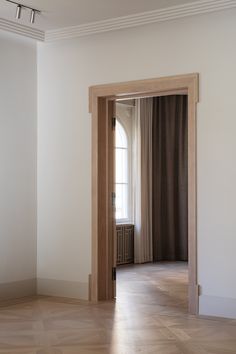 an open door leading into a room with wood floors and curtains on the windowsill