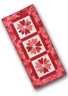 a red and white quilted table runner with four hearts on the center, in three squares