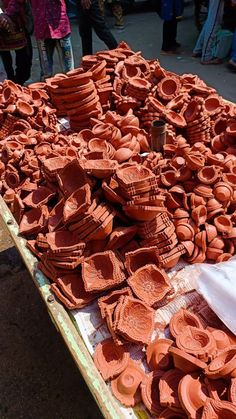 there are many clay pieces on the table for sale at this outdoor market, and people walking by