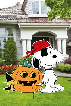 a snoopy pumpkin and jack - o'- lantern yard staker in front of a house