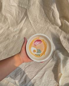 a person's hand holding a bowl with food in it on top of a bed