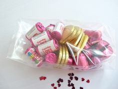 a plastic bag filled with lots of pink and gold foil wrapped candy hearts next to sprinkles