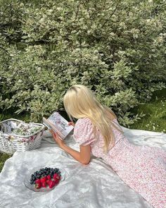 a woman reading a book while sitting on a blanket in front of a bush with berries