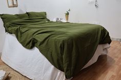 a bed with green sheets and pillows in a white room next to a wooden floor