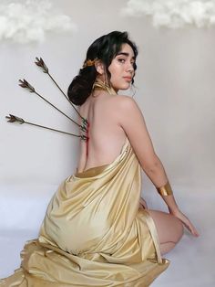 a woman in a gold dress sitting on the ground with arrows sticking out of her back