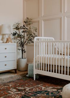 a white crib sitting next to a dresser with a potted plant in it