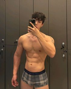 a shirtless man taking a selfie in front of lockers with his cell phone