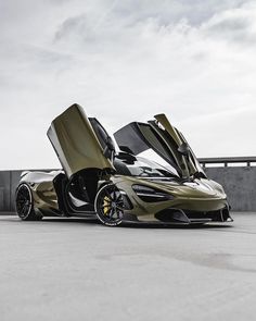 a gold colored sports car with its doors open on the road next to a concrete wall