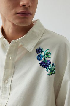 a man wearing a white shirt with colorful embroidered flowers on the chest and collarline