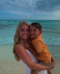 a woman holding a young boy on the beach at sunset with waves in the background