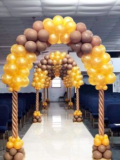 an archway decorated with gold and brown balloons in the shape of trees, along with two rows of blue chairs