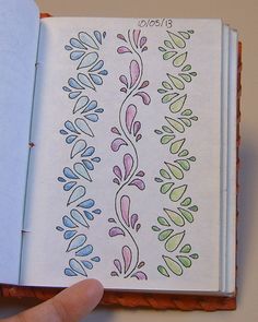 a hand holding an open notebook with designs on it