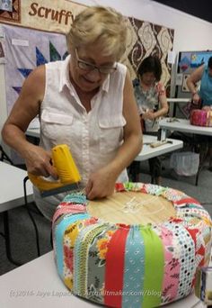 a woman is using a yellow sprayer on a colorful patchwork ottoman with people in the background