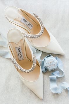 two pairs of wedding shoes on top of a white cloth with blue ribbons and a watch