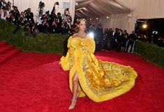 a woman in a yellow gown and fur stoler at the mete gala event