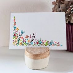 a white card with colorful flowers on it next to a wooden stamp and potted plant