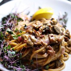 a white plate topped with pasta covered in sauce and mushrooms next to a lemon wedge