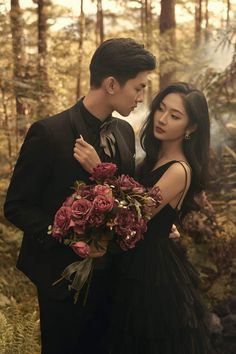 a man and woman standing in the woods with flowers on their chest, holding each other's shoulders